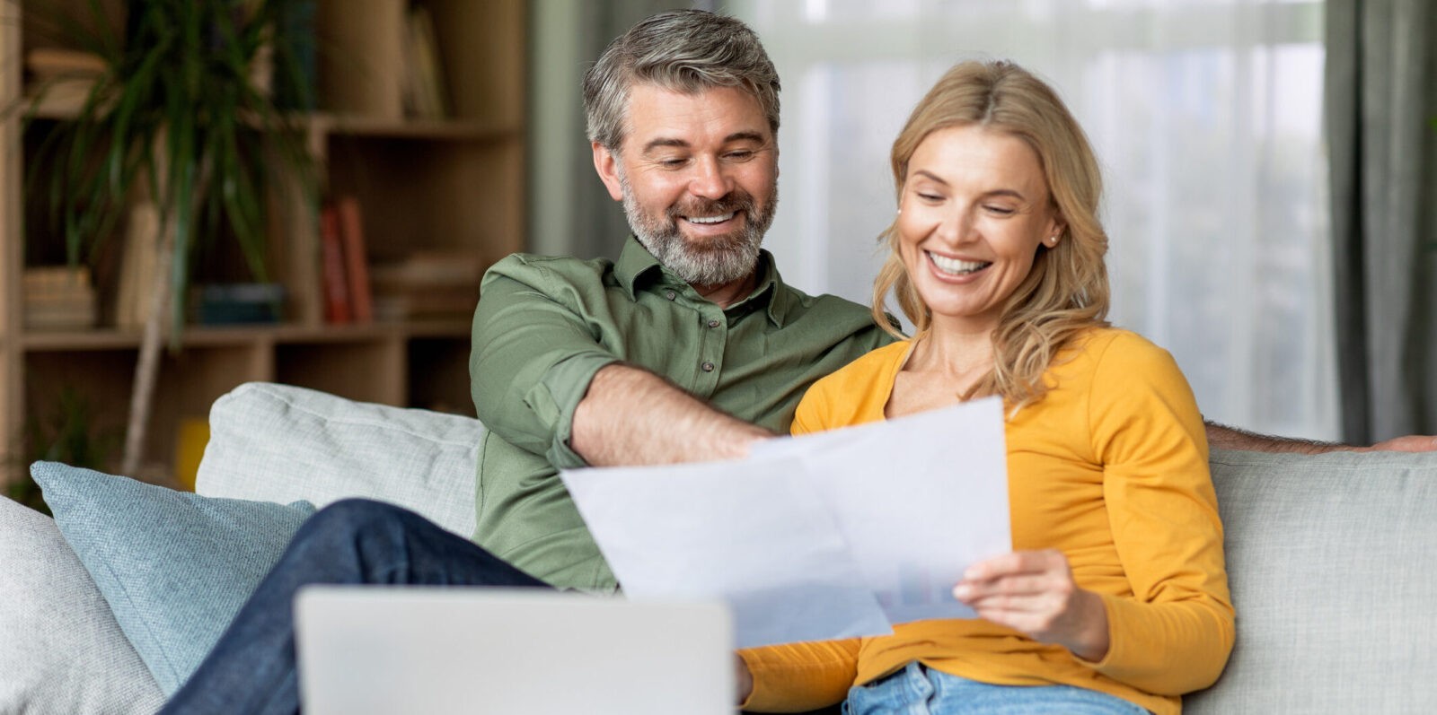 Family Insurance Concept. Happy Middle Aged Couple Reading Documents At Home, Smiling Mature Spouses Checking Financial Papers While Sitting Together On Couch In Living Room, Free Space