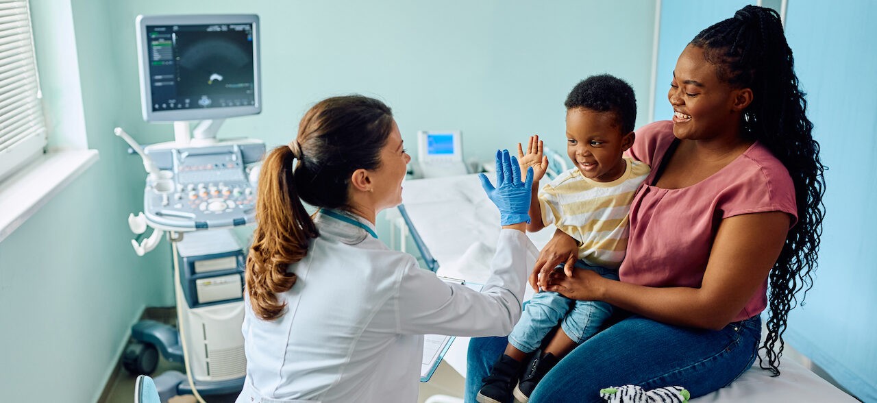 Happy African American boy giving high five to his pediatrician after medical examination at doctor's office.